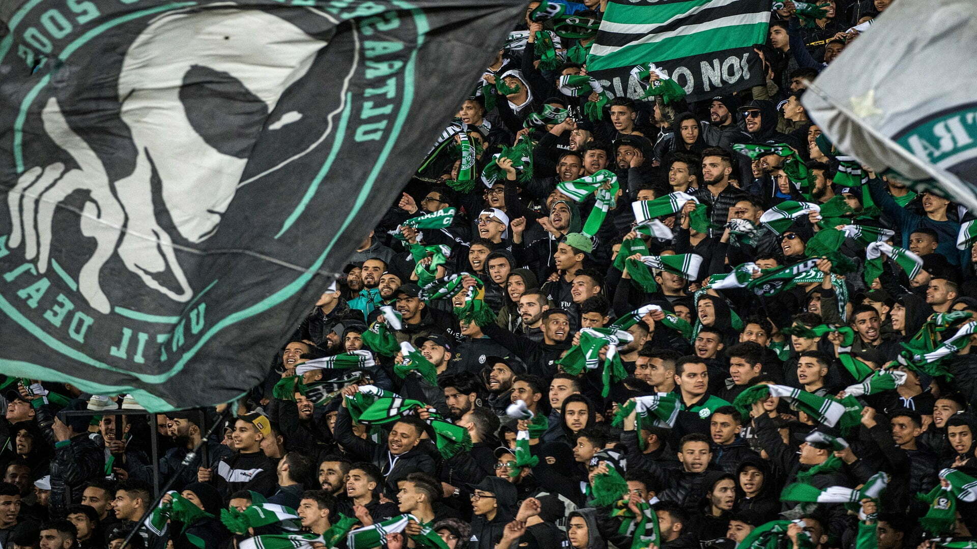 Supporters of Raja Club Athletic chant slogans and wave their flags as they attend a Moroccan Botola football match between Raja and Mouloudia Oujda in Casablanca on January 22, 2020. - From Casablanca to Algiers via Tunis, the chants belted out across football stadiums echo young North African fans' frustrations unrelated to the highs and lows of the beautiful game itself. Chants of "F'bladi delmouni!" ("Oppressed in my country!") at the demonstrations that have been commonplace in Algeria since last year originated on the noisy terraces manned by the ultras of Morocco's Raja Casablanca. (Photo by FADEL SENNA / AFP) (Photo by FADEL SENNA/AFP via Getty Images)